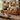 A rustic brown leather sofa with dark metal nailhead trim, set in a styled living room with a wooden coffee table, patterned rug, and framed wall art.