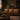 A rustic brown leather sofa with nailhead trim in a dark, cozy living room setting with a patterned rug, wooden coffee table, and a framed landscape painting on the wall.