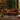 A classic brown leather Chesterfield sofa in a rustic, vintage-style living room setting with a wooden coffee table, potted plants, and a framed image on the wall