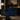 A deep blue velvet Chesterfield loveseat with nailhead trim, styled in a dark, elegant living room with a floor lamp, coffee table, and wall art.