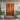 Wooden front door with decorative frame, potted plants, and doormat on a light gray wall.