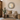 The round Flores mirror - with decorative white carved spots hanging above a rustic wooden bench with woven pillows and a beige throw blanket in a warm, neutral-toned entryway.