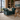 A plush teal velvet armchair with rolled arms and nailhead trim sits in a styled living room with a cream shag rug, wooden stool, bookshelves, and a large ocean painting on the wall.