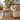 A rustic wooden end table with a single drawer and dark metal handle, styled in a bright, tropical-themed living room next to a cream leather sofa.