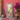 A tall full-length floor mirror with an ornate distressed whitewashed carved frame leans against a textured pink wall in a styled room. With a large vase of magenta flowers, a cushioned stool, and a patterned rug.