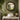 A round port hole style mirror mounted on a green tiled wall above a white vessel sink with a brass faucet in a styled bathroom setting.