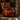 A brown leather wingback armchair with nailhead trim and turned wooden legs, styled in a rustic room next to a wooden barrel side table holding two glasses and a decanter.