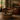 A warm, rustic living room scene featuring a brown leather sofa with vertical channel tufting, a round wooden coffee table in the foreground, a patterned area rug