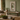 A wall mirror with a carved beige frame hangs above a rustic wooden console bench in a styled living room with a sofa, plants, books, and a coffee table.