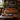 A brown leather loveseat sofa in a dark, stylishly decorated living room with a wooden coffee table, glassware, a potted palm, and framed wall art.
